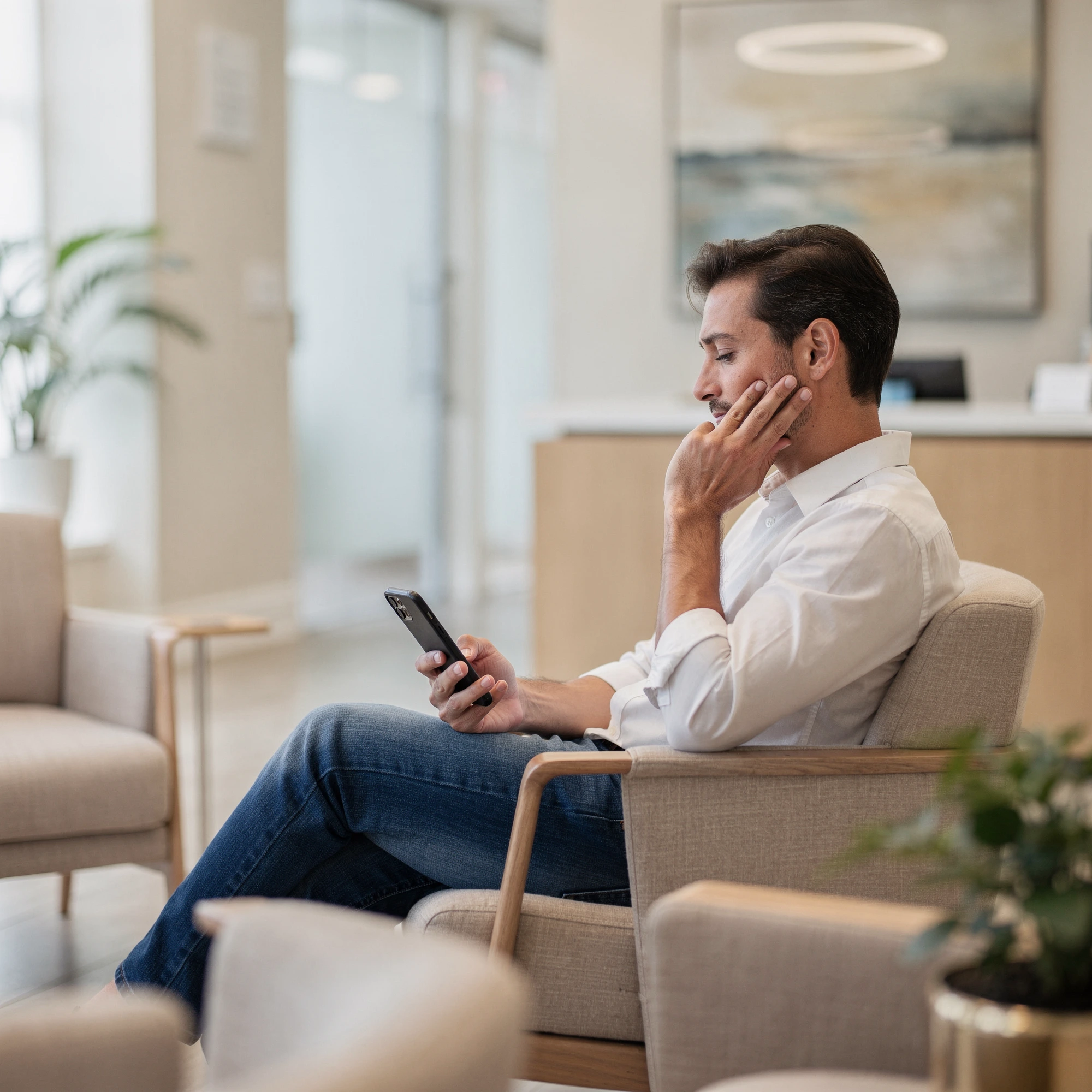 Man in waiting room holding his cheek in pain while looking at his phone